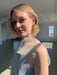 A woman with short blonde hair wears Noémiah’s Annie Earrings in a sunlit, minimalist room. She gazes gently at the camera, dressed in a sleeveless sheer top as sunlight streams through large industrial windows.