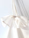 A white fabric bag, featuring a delicate, sheer white bow adorned with Swarovski crystal embellishments at its center, hangs against a white wall. This elegant bow adds a touch of sparkle and sophistication to the minimalist design of the Ariel Dress by Noémiah.