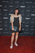 A woman in an Arlette Top featuring sheer puffed sleeves poses on the red carpet. Holding a clutch, she stands before a backdrop adorned with logos like NARS and CAFA. Her silk organza ensemble is complemented by white heels, and she beams with elegance. The top is designed by Noémiah.