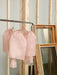 A wooden frame structure featuring two pastel pink fabric pieces, reminiscent of an Arlette Top by Noémiah, hangs gracefully on a metal rack. Next to it, several wooden-framed mirrors lean casually against the wall, reflecting elegance and style.