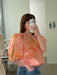 Une personne porte un haut Arlette — Floral Edit en organza de soie couleur pêche, à manches bouffantes et orné d'un motif floral orange, rentré dans un jean bleu.
