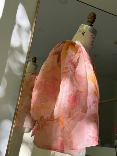 Noémiah Arlette Top — Floral Edit in sheer pink silk organza with a floral print, puffed sleeves, and scalloped hem edges on a dress form.