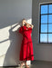 A person in the elegant, flowing Billie Dress by Noémiah poses gracefully against a sunlit white wall. Their shadow is cast on the surface, while a large window reveals a clear blue sky outside. The silk organza fabric of the dress catches the light beautifully, adding to the scene's allure.