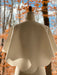 A white Camille Capelet by Noémiah is elegantly draped over a dress form, photographed outdoors. The background reveals a forest with bare trees and orange leaves, capturing the essence of an autumn bride's setting beneath a partly cloudy sky.