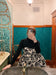 A person wearing a black top and the Capucine Classic Dress by Noémiah, which is a black and white patterned bustier mini dress with silk shoulder straps, takes a mirror selfie in a bathroom. The space features teal tiled walls and a vintage bathtub under a decorative ceiling light.