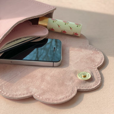 An open Noémiah card holder, featuring a pink cloud-shaped design with chic scalloped edges, showcases a smartphone, a floral-decorated lipstick, and a small notepad inside against a light background that highlights its stylish allure.