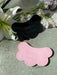 Two cloud-shaped leather card holders, featuring a unique scalloped design, one black and one pink, rest on a gray surface. Each card holder is embossed with VEINAGE x Noémiah. A white lily with light purple flowers adorns the top left corner.