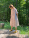 In a lush forest setting, an individual stands on a wooden platform wearing the loose-fitting Cécilia Striped Dress by Noémiah, paired with yellow shoes. Sunlight filters through the trees, casting gentle shadows on the ground and perfectly capturing the essence of relaxed femininity.