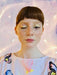 A person with short brown hair and freckled skin is wearing a Noémiah Célia Printed Dress featuring exclusive abstract patterns. Their eyes are adorned with glitter, and one eye is closed. The softly blurred background in pastel tones adds a dreamlike touch to this Estée Preda collaboration look.