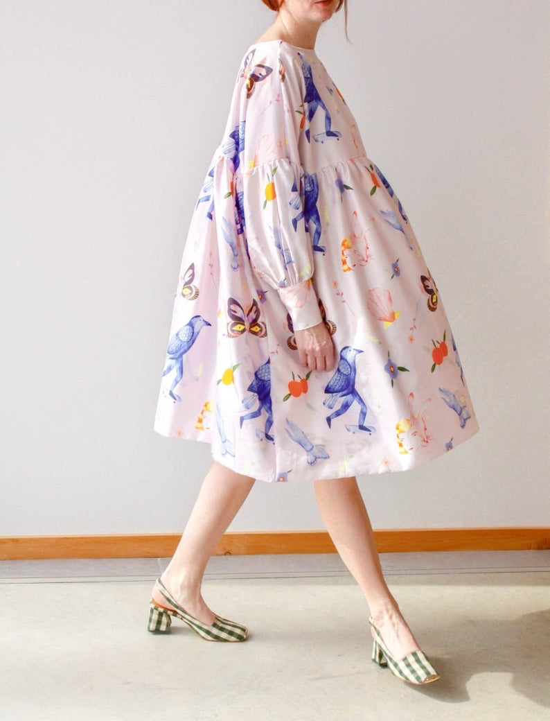 A person strolls on a light-colored floor, wearing striped high-heeled shoes and an exclusive Célia Printed Dress by Noémiah, adorned with colorful animal and insect prints, including birds and butterflies. This unique piece is part of the enchanting Estée Preda collaboration.