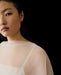 A woman with long dark hair wears the Noémiah Céline Silk Satin Dress — Bridal Edit and a gold earring, posed against a black background with only the left side of her face and upper body visible.