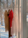 Three elegant dresses, including a Florence Silk Dress—Classic by Noémiah, hang on a rack by a sunlit window. The beige, red, and white garments are made of sheer silk organza. A snowy forest scene is visible through the glass outside.