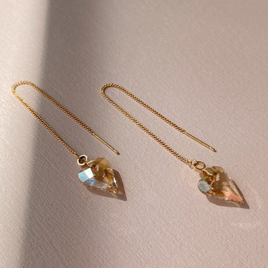 The Danielle Earrings by Noémiah feature gold threader design with 16K gold-plated heart-shaped Swarovski crystal pendants that glisten in the sunlight on a light surface.