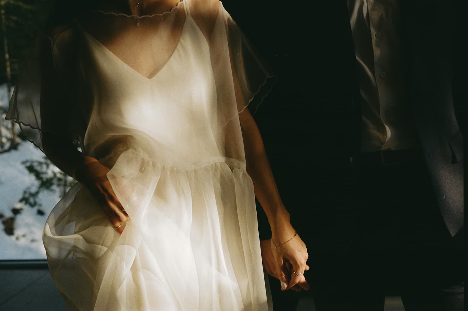 Woman wearing a sheer, flowing Noémiah embroidered Tulip dress, holding hands with a man in a dark suit.