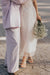 A couple embraces on a cobblestone street. One person wears a light purple suit, while the other, dressed in Noémiah's sheer white Embroidered Tulip Dress, holds a bouquet of white flowers. Their faces are out of view, capturing an intimate, serene moment.