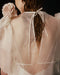 A person with wet hair is adorned in the Esperanza Maxi Dress — Bridal Edit by Noémiah, a handmade-to-order piece featuring delicate silk straps and a tied ribbon at the back, with a fabric flower on the shoulder. The image captures the back and part of their arm against a dark background.