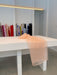 A peach-colored sheer fabric, reminiscent of the Esperanza Midi Dress made from organza silk by Noémiah, is draped over a white table in a bright room. Rolls of various colorful fabrics stand vertically against the wall in the background, suggesting future creations such as dresses with puffed sleeves.