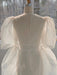 A dress form showcases the elegant Esperanza Midi Dress — Organza Silk from Noémiah, crafted with a delicate fabric and adorned with large puffed sleeves. The gown is cinched at the back with a ribbon, and the soft light streaming through the window accentuates its ethereal essence.
