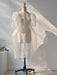 In a sunlit room, the Esperanza Midi Dress by Noémiah stands elegantly on a dress form, its sheer organza silk fabric with puffed sleeves catching the light. Shadows play across the white wall behind it, while a small plant sits gracefully on a nearby stand.