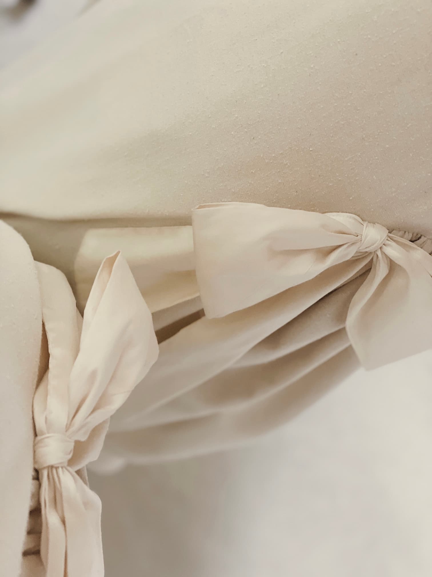 Close-up of beige fabric with decorative bows tied along the edges, achieving a soft and elegant look reminiscent of the Noémiah Esperanza Midi Dress in raw silk.