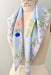 A light blue silk scarf, known as the Fleurs Coupées Scarf by Noémiah, with hand-painted floral designs drapes over a mannequin torso. This scarf, reminiscent of folk art, showcases pink, peach, and blue flowers with green leaves. The mannequin is labeled Superior Model Form Co., adding an elegant touch to this Estée Preda creation.