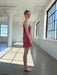 A young woman in the Noémiah Florence Lyocell Dress — Classic and white heels stands in a bright, spacious room with large windows casting geometric shadows. She looks at the camera, smiling softly.