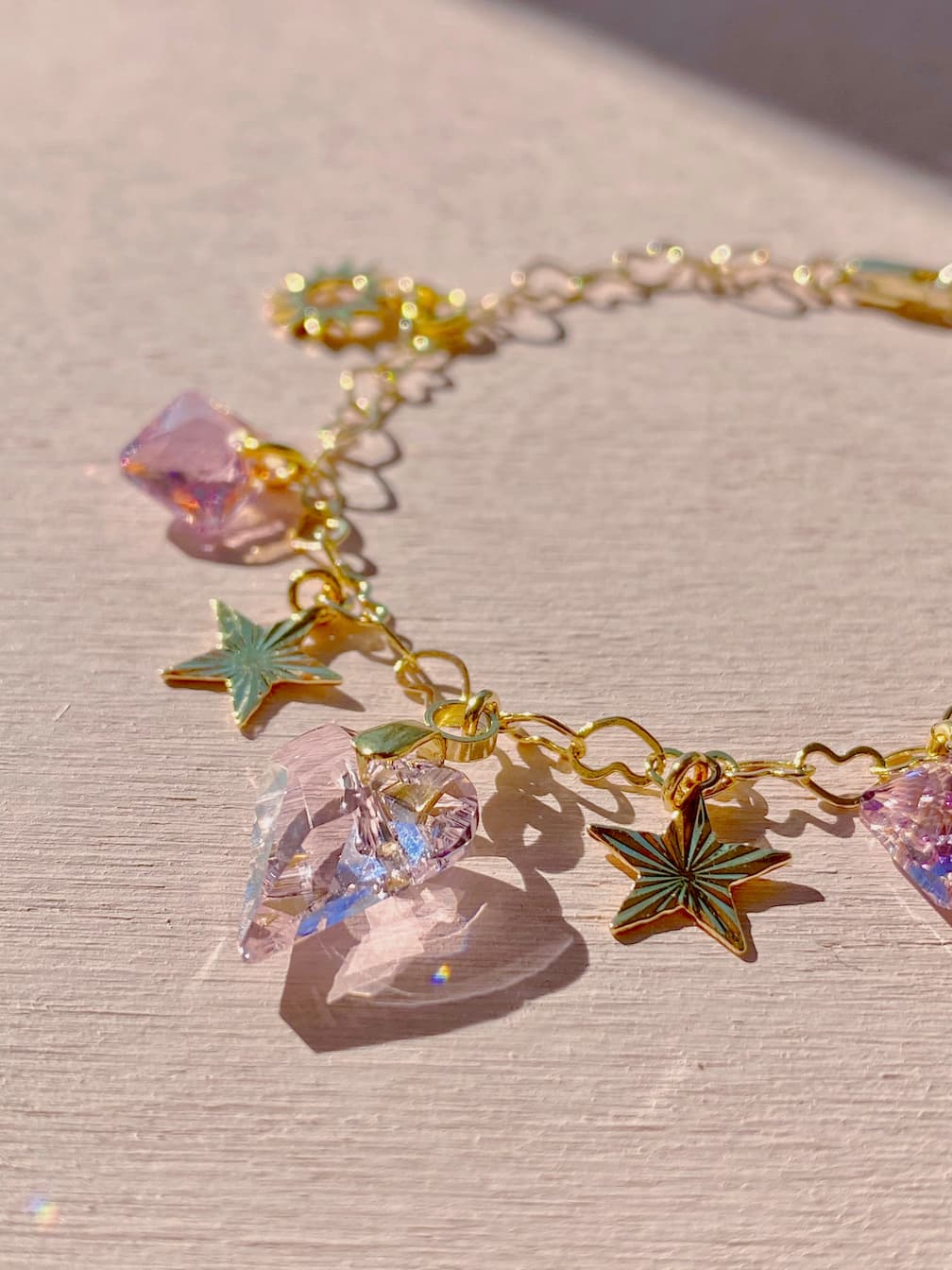 The Henriette Bracelet, from the brand Noémiah, is a gold chain bracelet with exquisite gold-plating and features charming Swarovski crystal heart and star charms. Elegantly displayed on a light surface, these crystals beautifully catch the light, highlighting their colorful and shiny appearance.