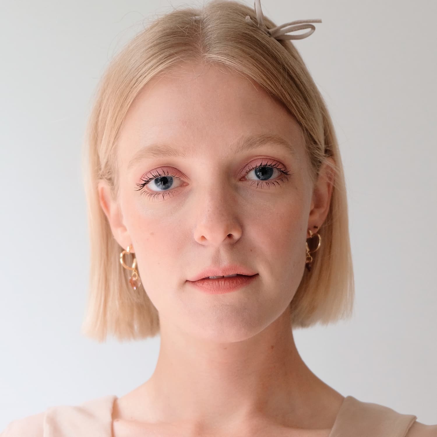 A person with short blonde hair, wearing a light-colored top and the tarnish-resistant Huguette Earrings from Noémiah, adorned with Swarovski crystals, looks directly at the camera with a neutral expression against a plain white background.