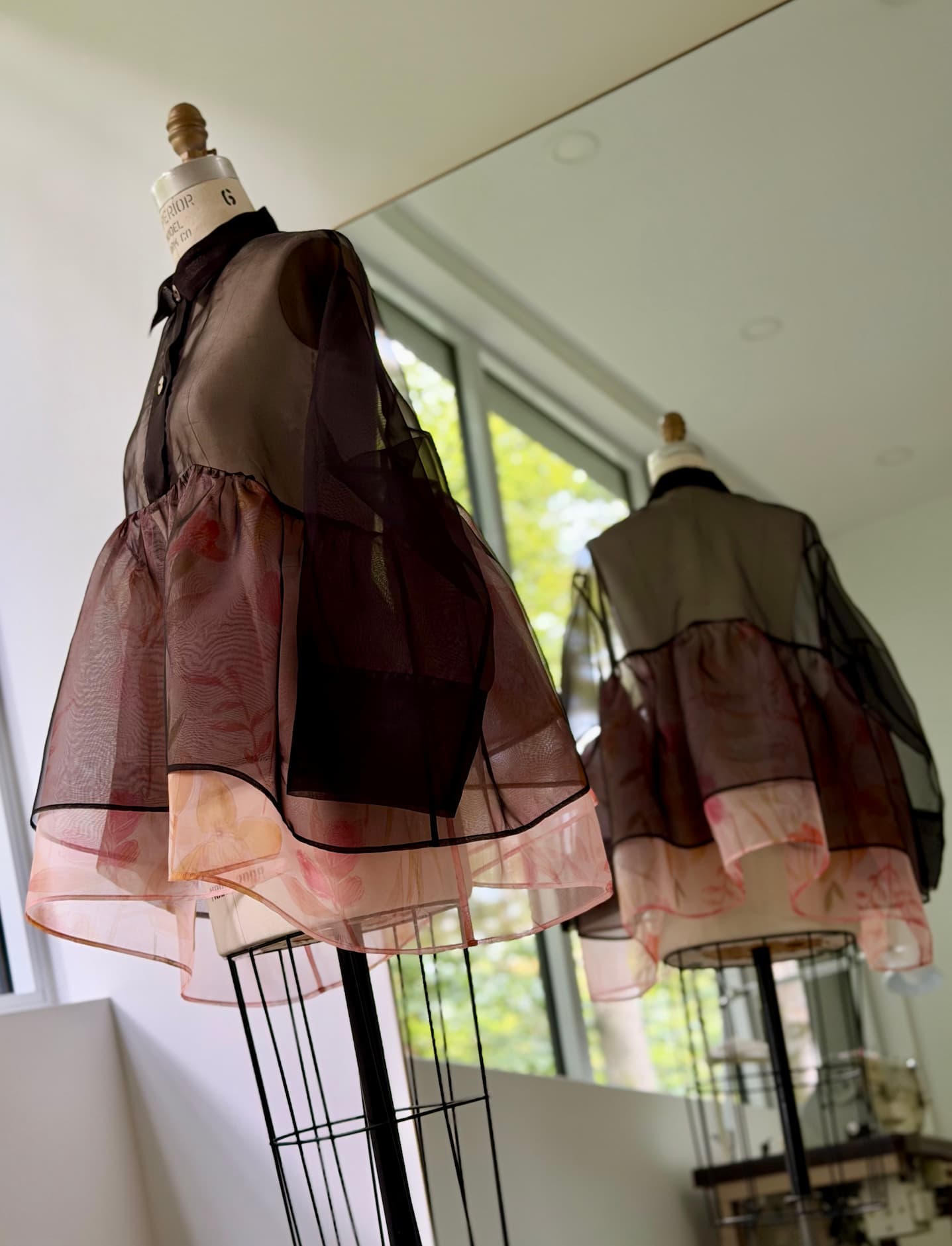 Haut Noémiah Iveth : un haut péplum transparent et sculptural, boutonné, avec un ourlet évasé en couches, orné d'un imprimé floral rouge, présenté sur un mannequin.