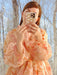A person in a Céline Floral Dress by Noémiah takes a selfie with a phone that has a cloud-patterned case. They're standing in front of a window with a blurred view of leafless trees in the background.