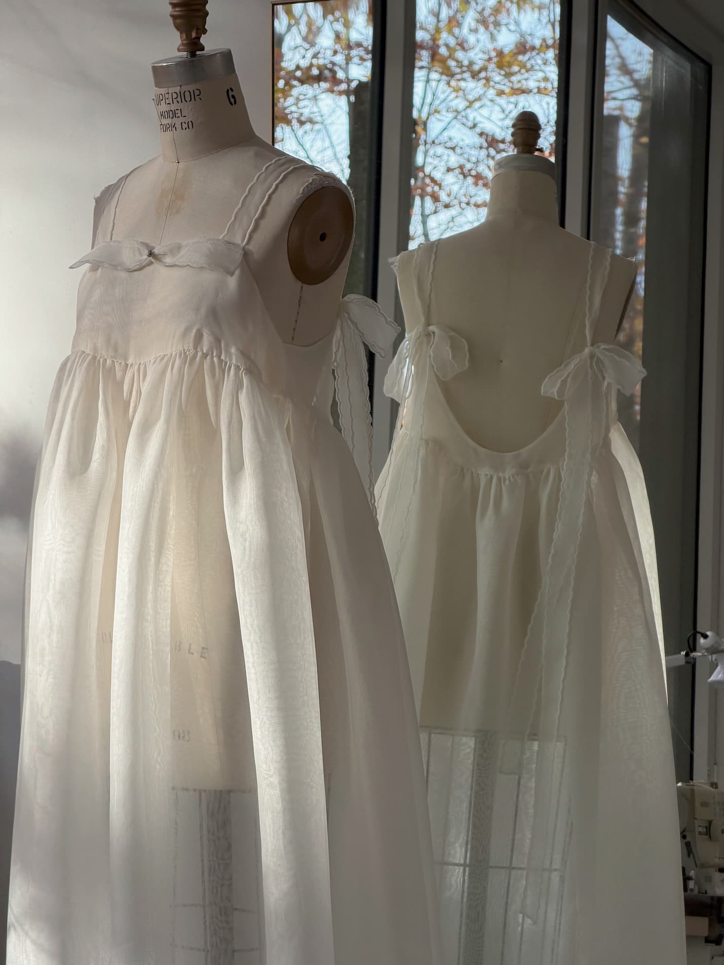 Two white silk organza Jeanne Dress — Bridal Edit slip dresses on dress forms, featuring spaghetti straps tied in bows and a low back design.