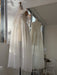 The Noémiah Jeanne Dress — Bridal Edit is a sheer white silk organza tiered dress with ribbon tie straps on a dress form, reflected in a large mirror.