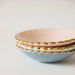 A set of three scalloped ceramic bowls from Noémiah, elegantly edged with gold trim, functions as a Jewelry Dish. The bowls come in pastel shades of pink, white, and blue and are featured against a simple background.