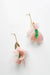 The Lili Earrings by Noémiah are beautifully designed with high-quality pink feathers and small green leaves, enhanced by oval gold-colored accents and delicate hooks. Silver-plated charms elegantly contrast against a white background, adding an exquisite touch to these lightweight earrings.