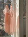 Two Lou Shirt Dresses, designed by Noémiah and crafted from sheer pink silk organza, hang on a slender bar in a sunlit room. They sway gently in the breeze, casting soft shadows on the wall. Outside, barren trees stand against the winter scene visible through the window.