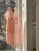Two Lou Shirt Dresses, designed by Noémiah and crafted from sheer pink silk organza, hang on a slender bar in a sunlit room. They sway gently in the breeze, casting soft shadows on the wall. Outside, barren trees stand against the winter scene visible through the window.