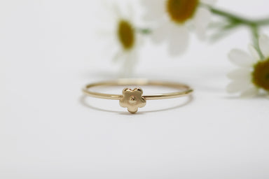 The Marguerite Ring by Noémiah is a delicate piece crafted in solid gold, showcasing a small flower design at its center, elegantly displayed against a softly blurred backdrop of white daisies.