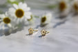 Marguerite Solid Gold Earrings by Noémiah rest on a marble surface, surrounded by blurred white daisies, creating a soft and elegant composition.