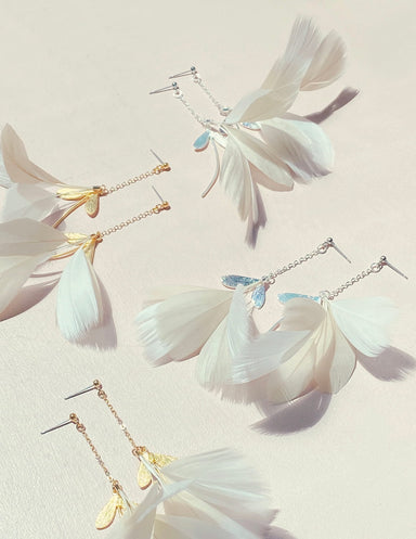 Introducing the Marie Earrings by Noémiah: a set of exquisite earrings adorned with premium feather-like accents and elegant metallic charms. These earrings are designed with gold-filled hooks and slender chains, achieving a lightweight and ethereal look, all showcased beautifully on a soft, neutral background.