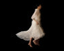A woman in the Marine Dress by Noémiah—crafted from translucent silk organza with lantern sleeves—walks barefoot against a black background, her slightly blurred figure evoking motion and grace.