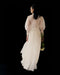 A woman with dark, wet hair faces away from the camera against a black background, wearing the Marine Dress by Noémiah—a sheer silk organza design with lantern sleeves—while holding white flowers in her left hand.