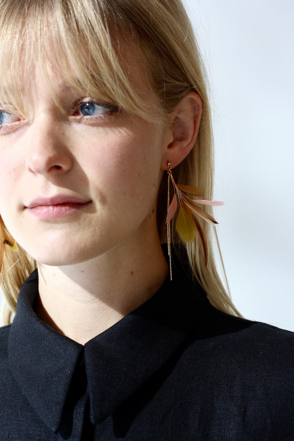 A person with blonde hair is wearing a black top and the vibrant, large Nicole Earrings by Noémiah. They are gazing away from the camera against a plain background.