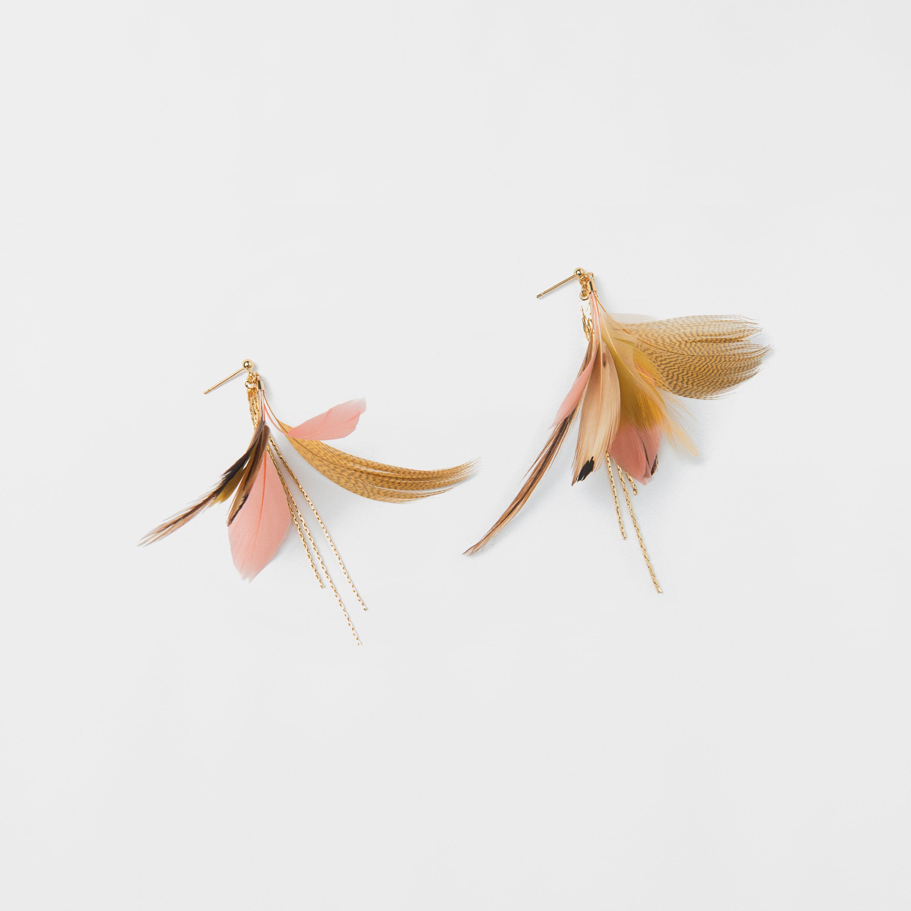 Introducing the Nicole Earrings by Noémiah: a pair of elegant clip-on earrings featuring delicate feather details in shades of gold, pink, and beige. The design is enhanced with a 16K gold-plated chain detail and set against a plain white background.