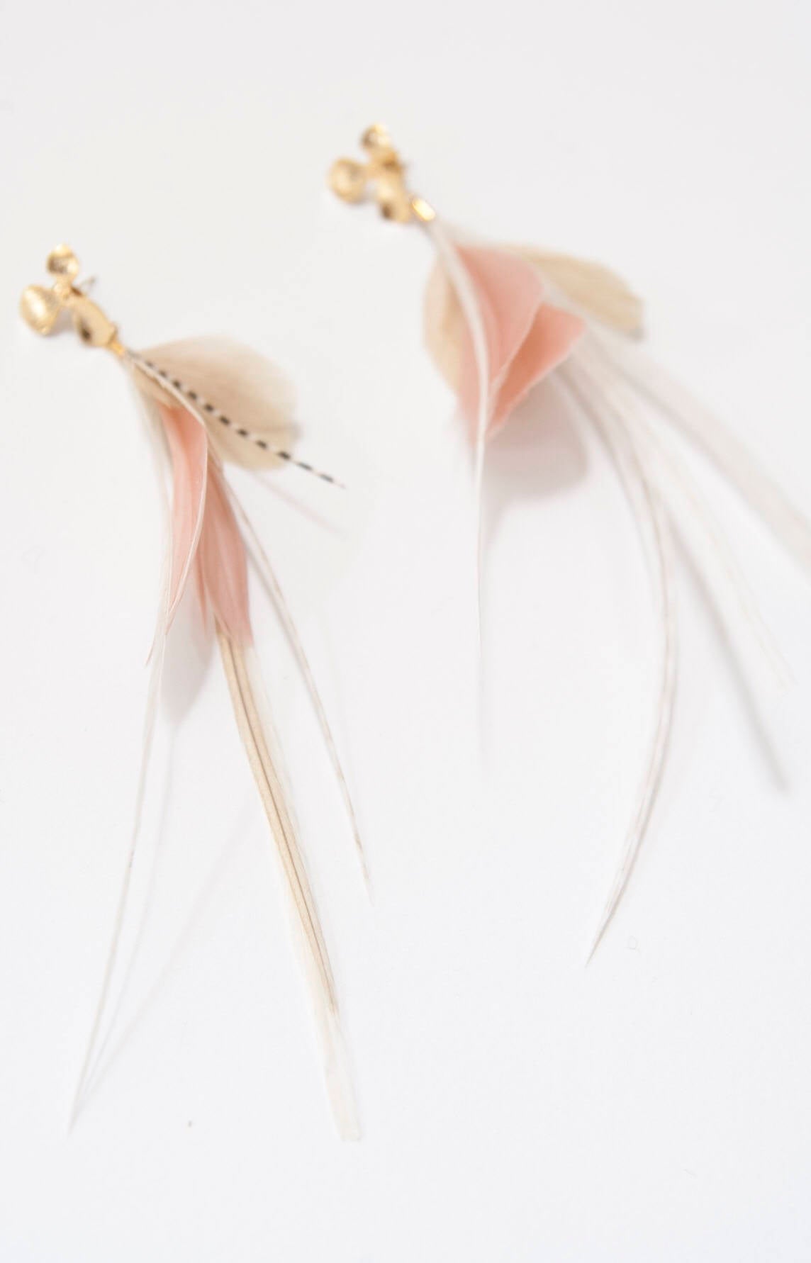 Close-up of two Pénélope Earrings by Noémiah featuring delicate, soft pink and cream feathers with gold studs. The high-quality feathers are layered and slightly curved, creating a graceful, flowing appearance against a plain white background.