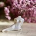 A Porcelain Bud Vase by Noémiah, shaped like a reclining human torso, cradles delicate pink flowers. It is set on a wooden surface, enhancing your space with its handcrafted charm, as additional pink flowers create a gentle blur in the background.