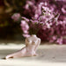 A petite Porcelain Bud Vase by Noémiah, designed in the elegant form of a reclining female torso, cradles delicate pink flowers. The softly blurred background hints at matching pink blooms, creating a tranquil and artistic scene ideal for elevating a self-care ritual with its handcrafted charm.