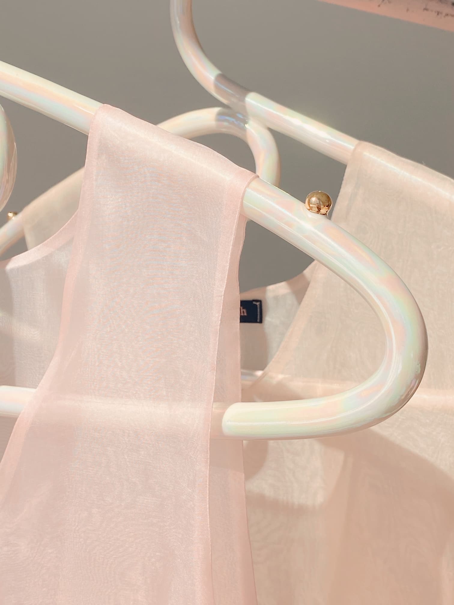 A close-up of the Porcelain Hanger by Noémiah, showcasing sheer, pale pink fabric draped elegantly. The iridescent luster of the translucent and delicate material evokes the elegance of wedding dresses, while soft lighting enhances a gentle and serene atmosphere.