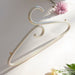 A Porcelain Hanger by Noémiah stands upright against a cream backdrop with soft lighting, its iridescent luster gently catching the eye. Surrounding it are fresh flowers: a pink chrysanthemum, a yellow marigold, and white roses, adding a touch of color and elegance reminiscent of handcrafted porcelain.