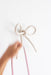 A hand holding pink cables reaches towards the Porcelain Hook by Noémiah, designed like a bow, cleverly utilizing wall space against the plain white backdrop.