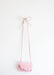 A beautifully handcrafted small pink purse with a scalloped flap elegantly hangs from Noémiah's Porcelain Hook on a white wall. The strap is artfully tied into a bow at the top, securely suspended from the delicate hook.